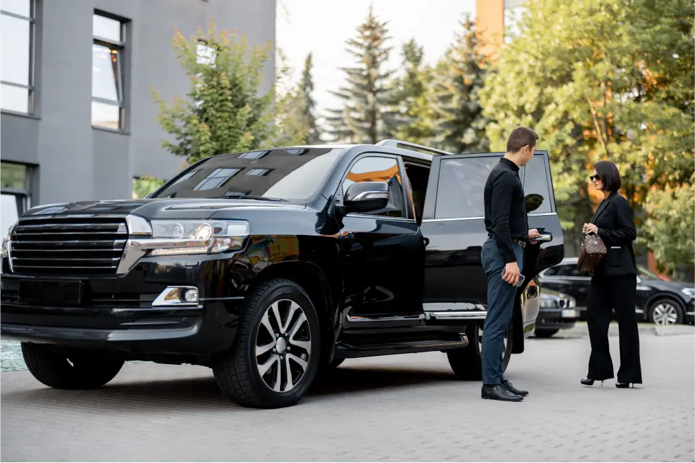 Chauffeur opening door of luxury black SUV for female passenger
